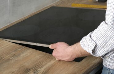 A young repairman installs a black induction hob in a modern white Scandinavian style kitchen