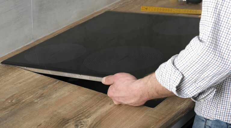 A young repairman installs a black induction hob in a modern white Scandinavian style kitchen